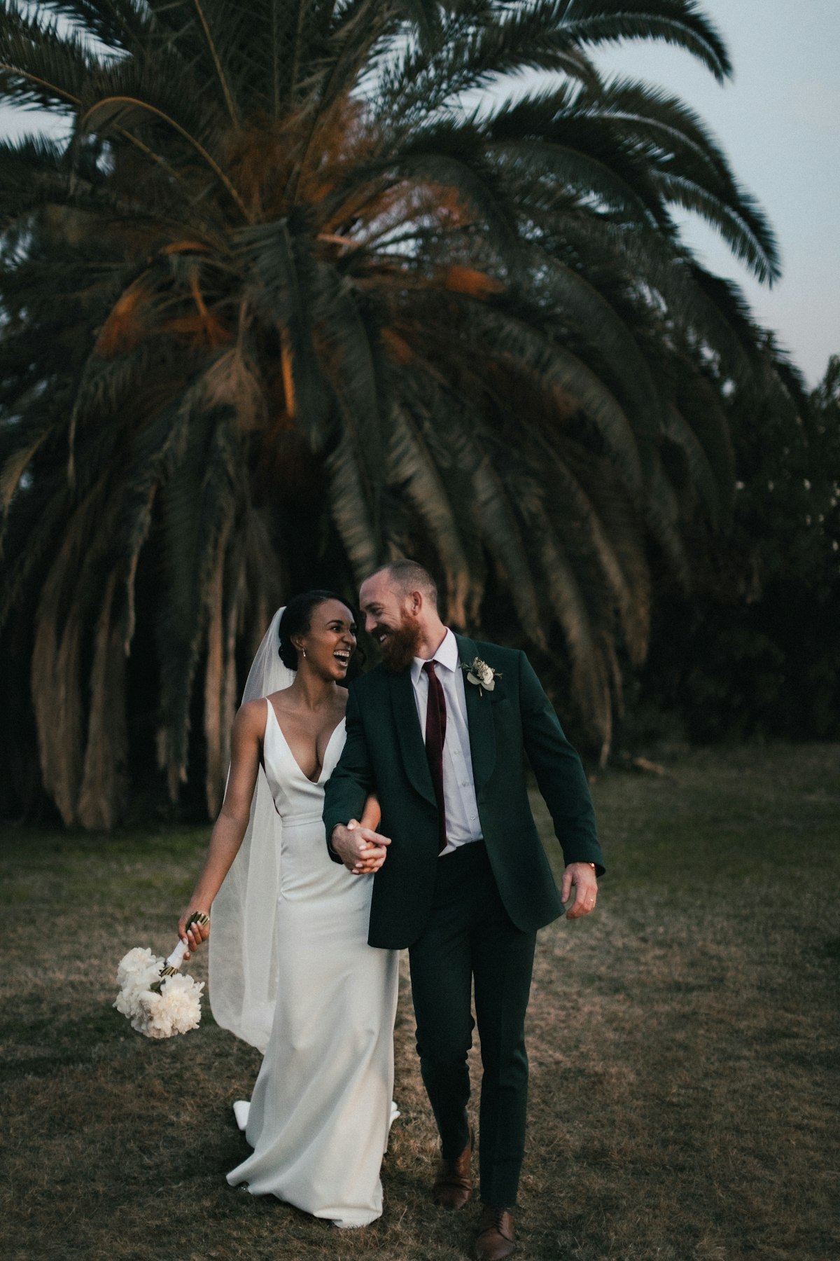 A smiling bride and groom holding hands outdoors on their wedding day