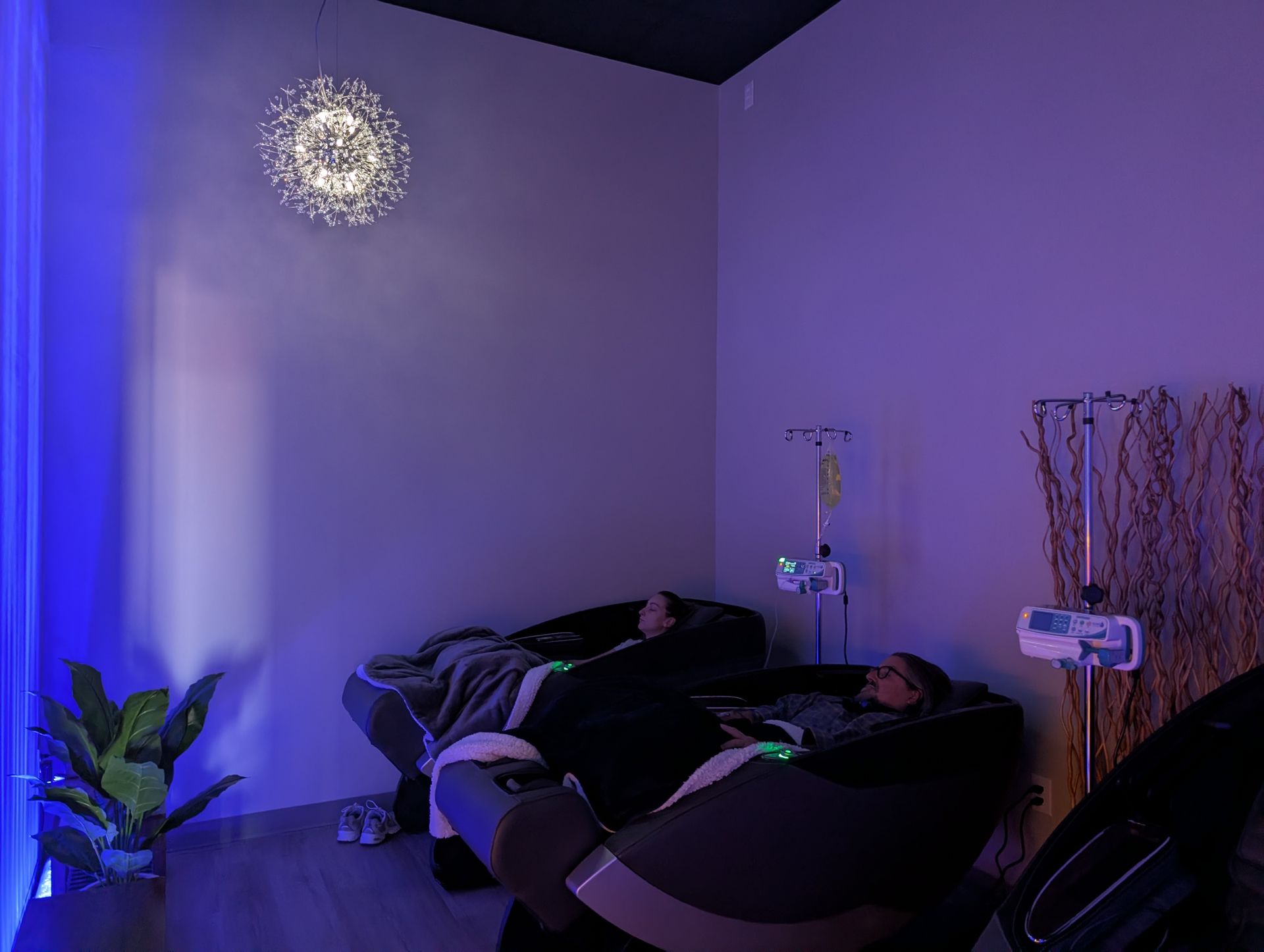 Two clients relaxing in zero-gravity massage chairs under cozy blankets while receiving IV therapy in the dimly lit, ambient-lit VIP lounge